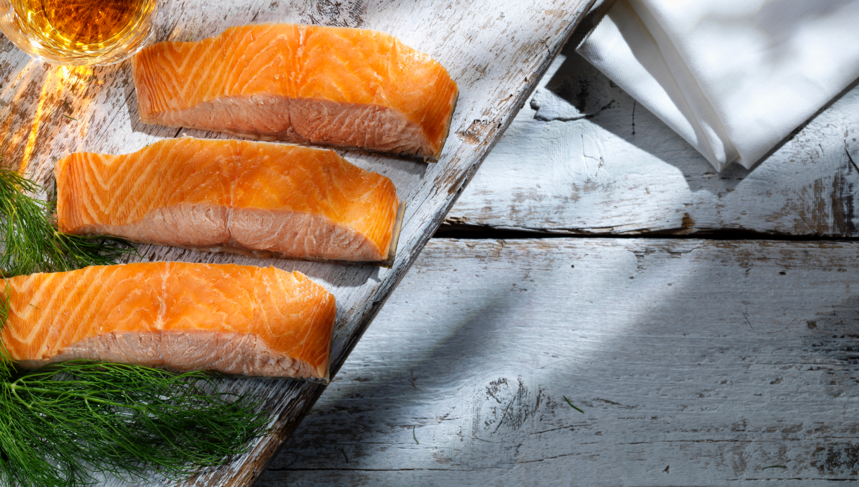 Three fillets of salmon laid out on a serving board with a few sprigs of fresh dill arranged beside them.