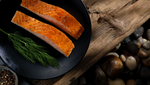 Two fillets of salmon with cracked black pepper and some fresh dill, beautifully presented on a black dinner plate.